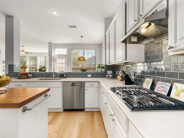 kitchen with a sink, butcher block counters, under cabinet range hood, stainless steel appliances, and visible vents