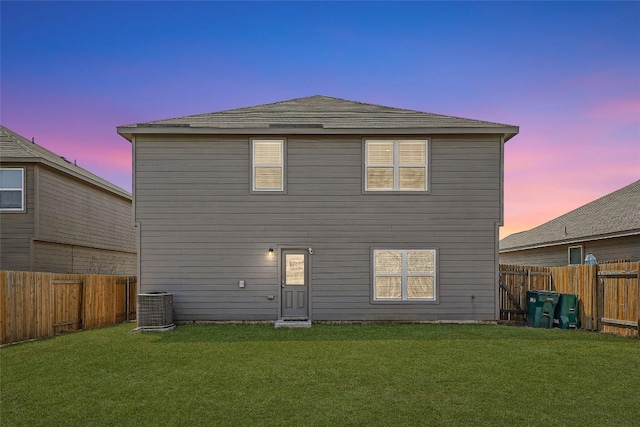 back of house at dusk featuring a fenced backyard, central AC, and a yard