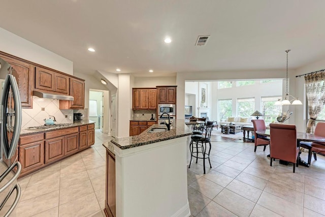 13229 Country Trails Ln, Austin, TX 78732 - kitchen with appliances with stainless steel finishes, under cabinet range hood, dark stone countertops, backsplash, and brown cabinets