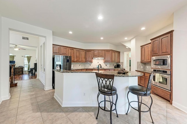13229 Country Trails Ln, Austin, TX 78732 - kitchen featuring appliances with stainless steel finishes, a kitchen island with sink, backsplash, dark stone counters, and recessed lighting