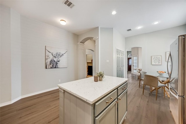 2974 Overland St, Round Rock, TX 78681 - kitchen featuring arched walkways, freestanding refrigerator, gray cabinetry, wood finished floors, and a center island