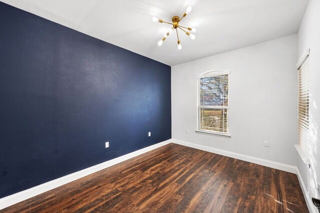 spare room featuring baseboards, wood finished floors, and a chandelier