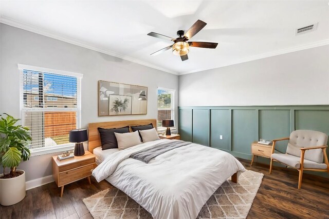 bedroom featuring a ceiling fan, ornamental molding, dark wood finished floors, visible vents, and a decorative wall
