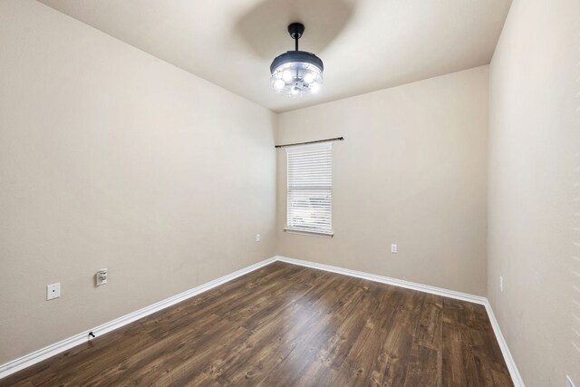 spare room featuring dark wood-type flooring, baseboards, and a chandelier