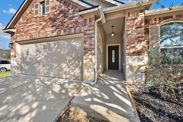 doorway to property with driveway, a garage, and brick siding