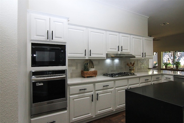 kitchen featuring decorative backsplash, crown molding, white cabinets, under cabinet range hood, and stainless steel appliances