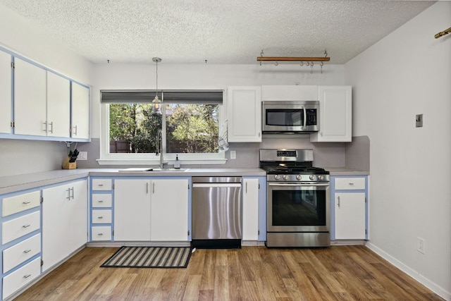 5304 Harvest Ln, Austin, TX 78745 - kitchen featuring appliances with stainless steel finishes, a sink, wood finished floors, a textured ceiling, and white cabinets