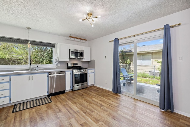 5304 Harvest Ln, Austin, TX 78745 - kitchen with appliances with stainless steel finishes, a sink, a textured ceiling, light wood finished floors, and white cabinetry