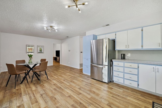 kitchen with a textured ceiling, visible vents, light countertops, light wood-style flooring, and freestanding refrigerator