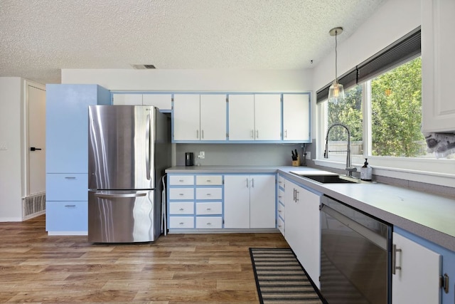 5304 Harvest Ln, Austin, TX 78745 - kitchen featuring appliances with stainless steel finishes, a sink, a textured ceiling, light wood finished floors, and white cabinetry
