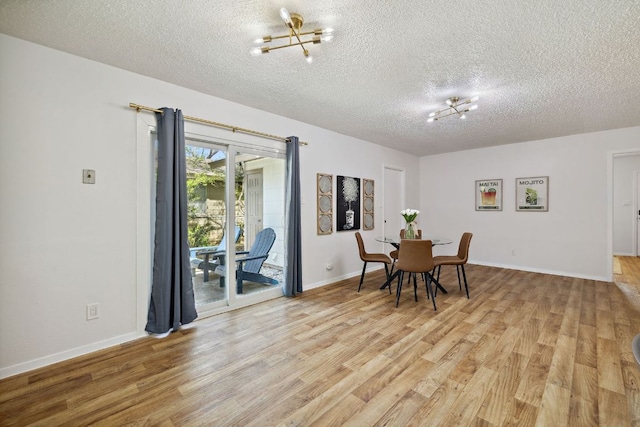 dining area featuring baseboards, a textured ceiling, an inviting chandelier, and light wood-style floors