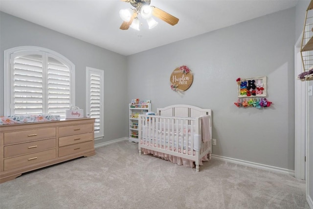 bedroom with a nursery area, baseboards, a ceiling fan, and light colored carpet