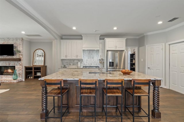 kitchen featuring a sink, stainless steel fridge, custom range hood, and dark wood finished floors