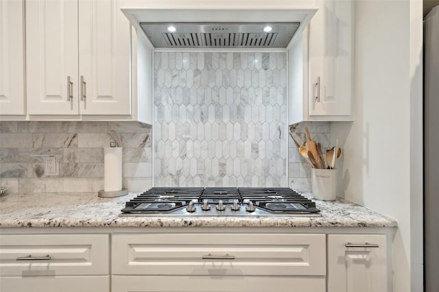 kitchen featuring stainless steel gas cooktop, white cabinets, backsplash, and wall chimney range hood