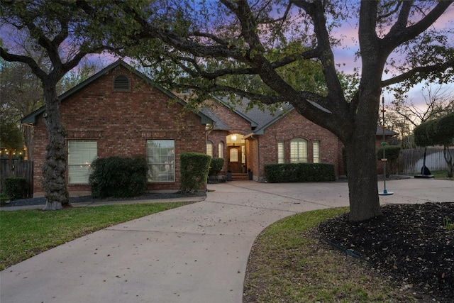 view of front of property with brick siding, fence, and curved driveway
