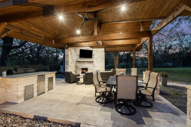 view of patio featuring exterior kitchen, a gazebo, a bar, fence, and an outdoor living space with a fireplace