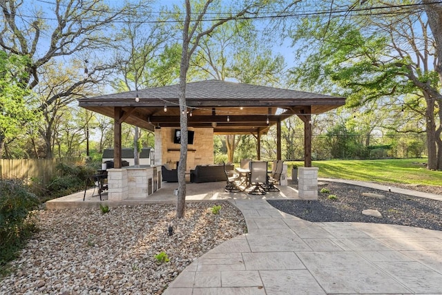 view of patio featuring fence, an outdoor stone fireplace, and a gazebo