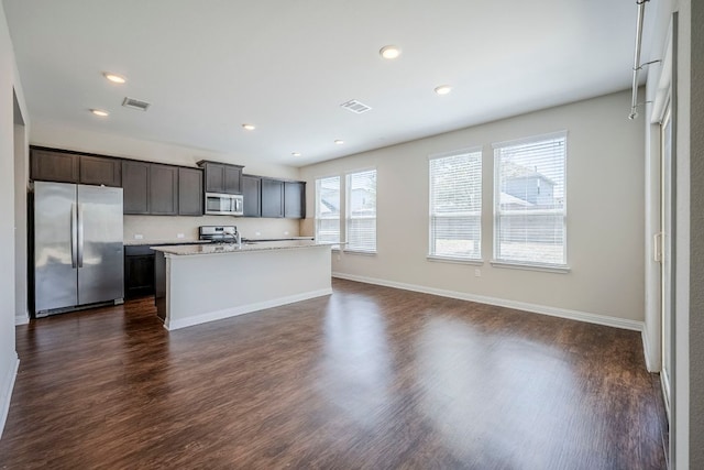 8017 Turnberry Ln, Austin, TX 78744 - kitchen featuring appliances with stainless steel finishes, a kitchen island with sink, dark wood finished floors, recessed lighting, and baseboards