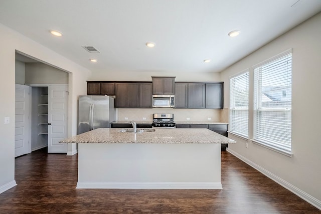 8017 Turnberry Ln, Austin, TX 78744 - kitchen featuring appliances with stainless steel finishes, a sink, an island with sink, dark brown cabinetry, and dark wood-type flooring