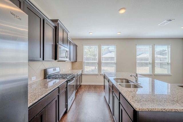 8017 Turnberry Ln, Austin, TX 78744 - kitchen with appliances with stainless steel finishes, a sink, wood finished floors, a kitchen island with sink, and decorative backsplash