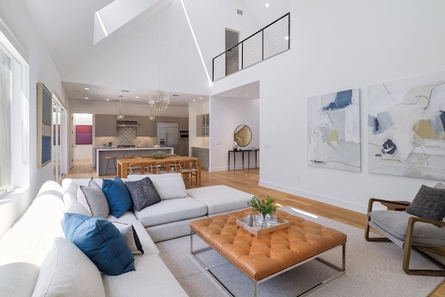 living room with baseboards, high vaulted ceiling, a skylight, and light wood finished floors