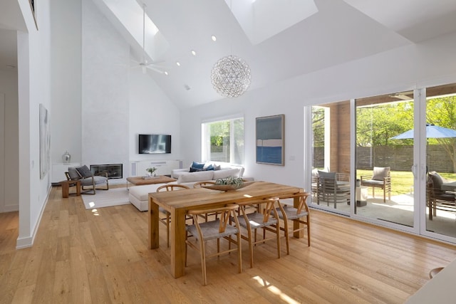 dining space featuring a fireplace, high vaulted ceiling, light wood-type flooring, baseboards, and a skylight