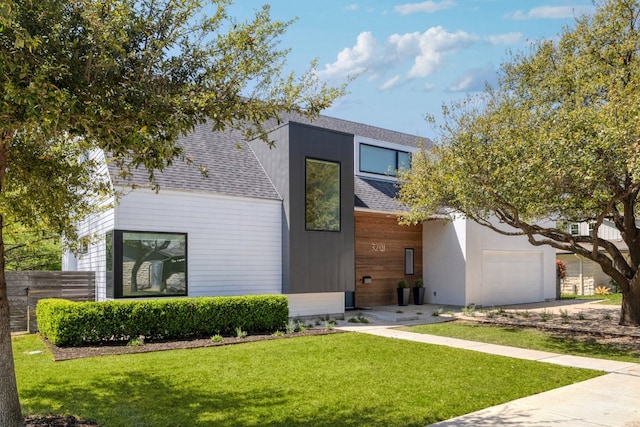 contemporary house with fence, a front lawn, an attached garage, and roof with shingles