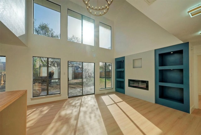 1701 Indian Camp Trl, Round Rock, TX 78681 - unfurnished living room featuring built in features, wood finished floors, a high ceiling, a chandelier, and a glass covered fireplace