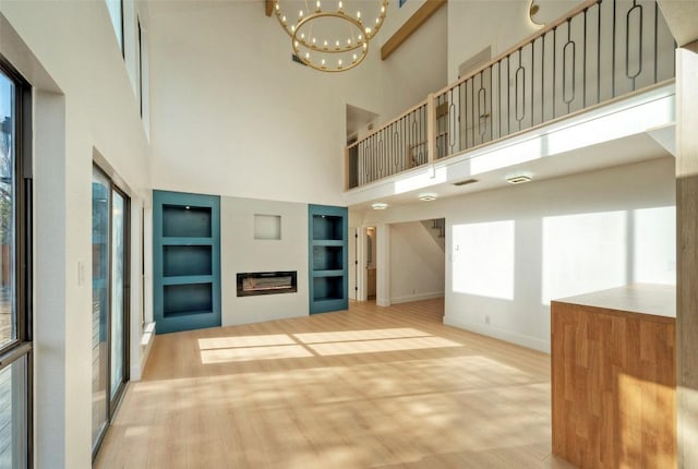 1701 Indian Camp Trl, Round Rock, TX 78681 - unfurnished living room with wood finished floors, built in shelves, a towering ceiling, a chandelier, and healthy amount of natural light