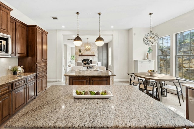 1420 Mirador, Leander, TX 78641 - kitchen featuring a center island, stainless steel microwave, backsplash, a lit fireplace, and light stone counters
