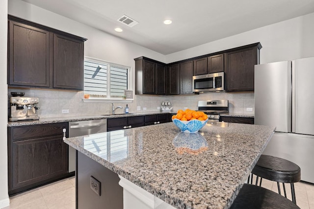 217 Timber Brook Dr, Hutto, TX 78634 - kitchen with appliances with stainless steel finishes, light stone countertops, a breakfast bar area, dark brown cabinets, and light tile patterned floors
