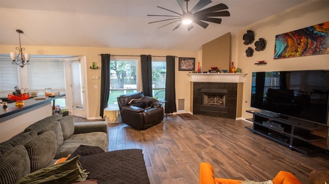 living area with baseboards, ceiling fan with notable chandelier, vaulted ceiling, a fireplace, and wood finished floors