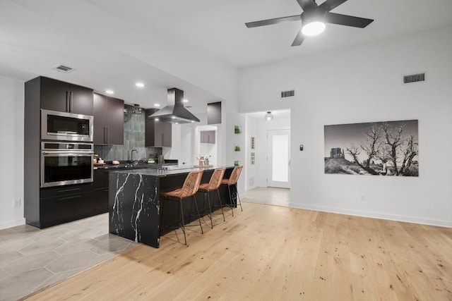 3503 Gable Dr, Austin, TX 78759 - kitchen featuring stainless steel appliances, island exhaust hood, dark cabinetry, a kitchen breakfast bar, and tasteful backsplash
