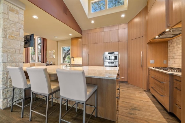 101 Knarr St, Austin, TX 78734 - kitchen featuring stainless steel appliances, tasteful backsplash, a breakfast bar area, light stone countertops, and wood finished floors