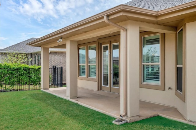 entrance to property featuring a patio area, roof with shingles, a lawn, and stucco siding