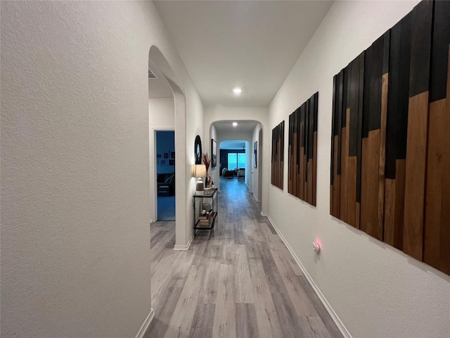 7900 Nightwing Rd, Austin, TX 78724 - hallway with baseboards, light wood-type flooring, arched walkways, and a textured wall