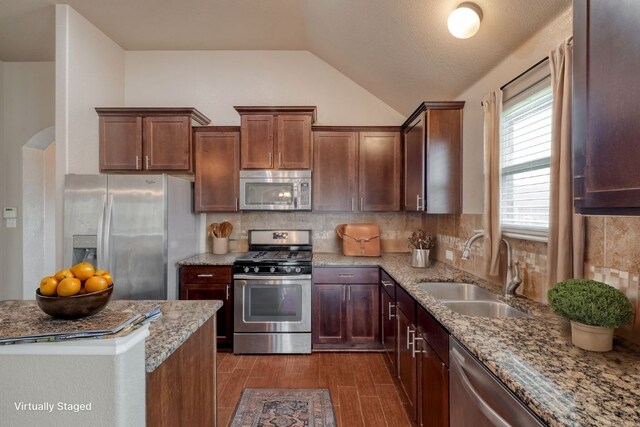 kitchen featuring appliances with stainless steel finishes, a sink, vaulted ceiling, tasteful backsplash, and light stone counters