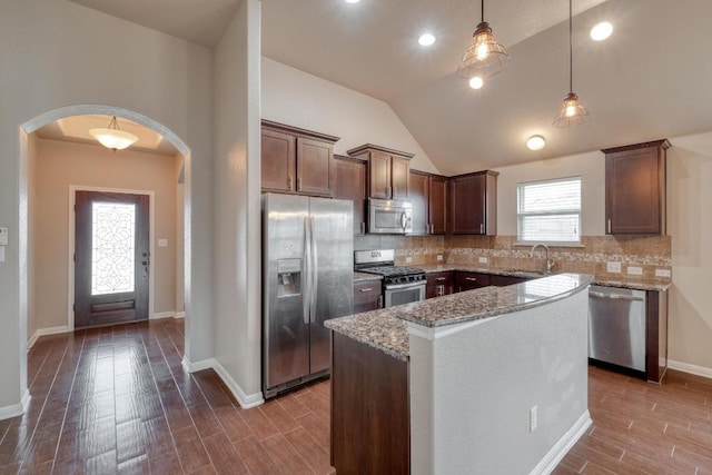 kitchen with appliances with stainless steel finishes, a sink, arched walkways, light stone counters, and dark wood-type flooring