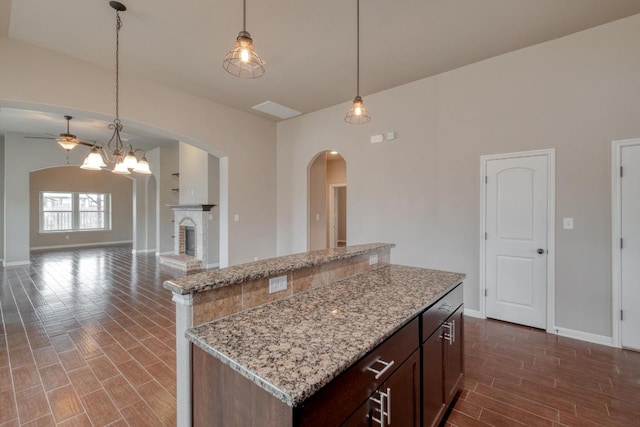 5660 Sabbia Dr, Round Rock, TX 78665 - kitchen with arched walkways, ceiling fan, a fireplace, pendant lighting, and dark wood-style flooring