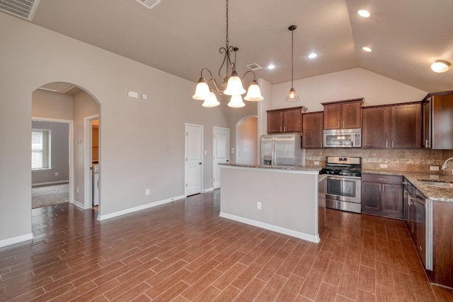 kitchen featuring appliances with stainless steel finishes, arched walkways, a sink, decorative backsplash, and lofted ceiling