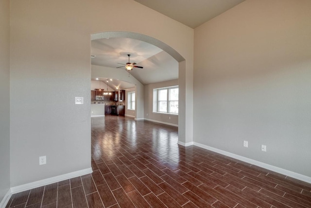 spare room with a ceiling fan, lofted ceiling, baseboards, dark wood finished floors, and arched walkways