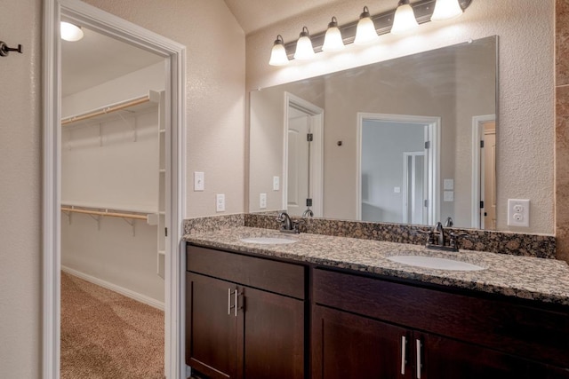 bathroom featuring a spacious closet, double vanity, and a textured wall