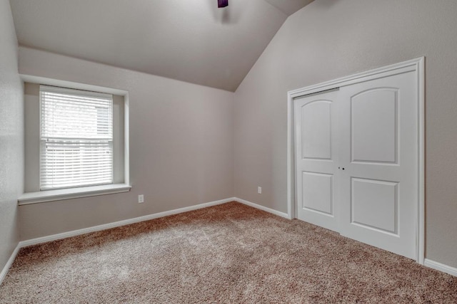 unfurnished bedroom with lofted ceiling, carpet floors, a closet, baseboards, and a ceiling fan
