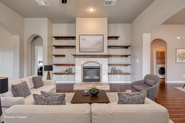 living room featuring arched walkways, baseboards, a glass covered fireplace, and washer / dryer