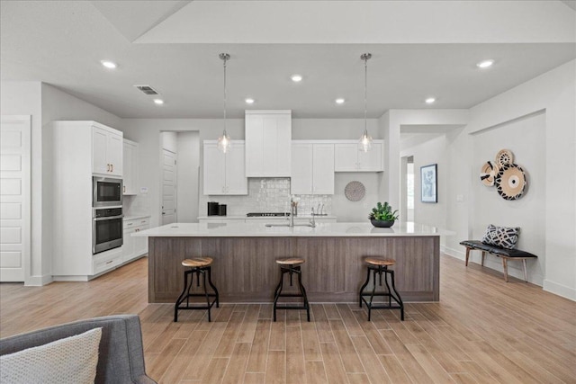 506 Diamondleaf Dr, Buda, TX 78610 - kitchen with appliances with stainless steel finishes, white cabinets, light wood-style floors, decorative backsplash, and a large island with sink