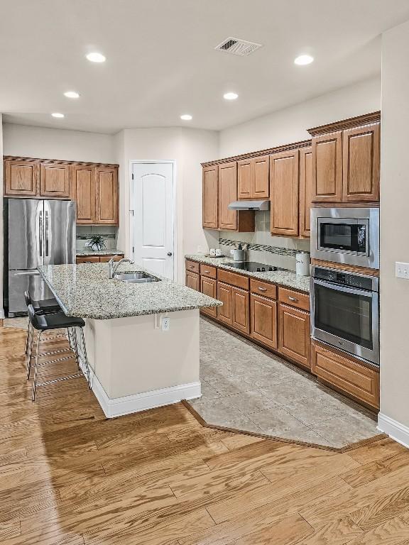 10601 Twisted Elm Dr, Austin, TX 78726 - kitchen featuring appliances with stainless steel finishes, brown cabinets, light wood finished floors, light stone counters, and recessed lighting