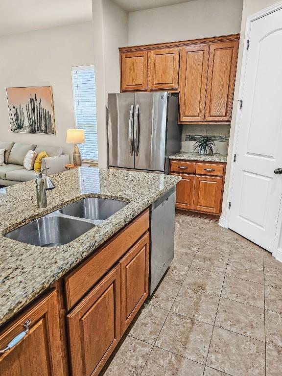 10601 Twisted Elm Dr, Austin, TX 78726 - kitchen featuring stainless steel appliances, brown cabinetry, light stone countertops, open floor plan, and light tile patterned floors