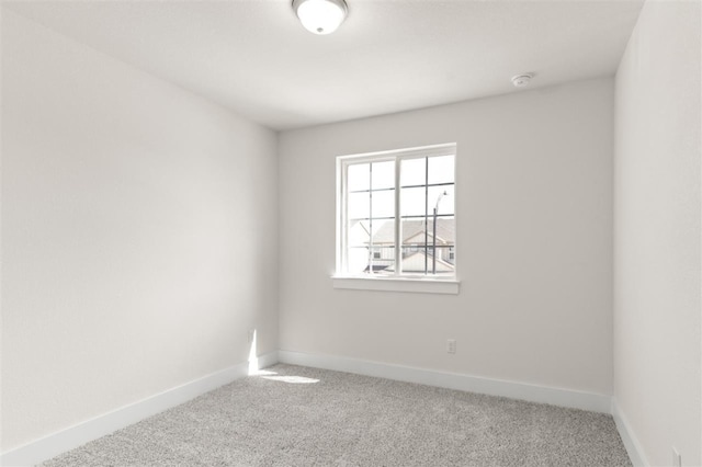 carpeted empty room featuring baseboards and a smoke detector