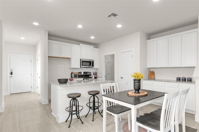 kitchen featuring appliances with stainless steel finishes, white cabinets, a kitchen island with sink, light stone counters, and recessed lighting