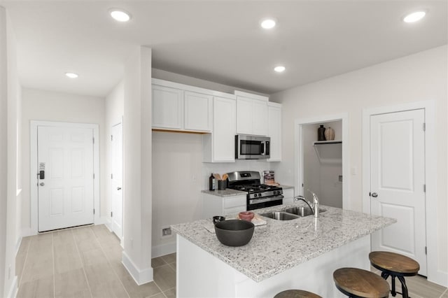 kitchen featuring appliances with stainless steel finishes, a sink, white cabinets, a breakfast bar area, and light stone counters